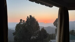 A view from a window overlooking a mountainous landscape during sunset.