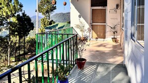 A building with a covered porch, a green railing, and potted plants.