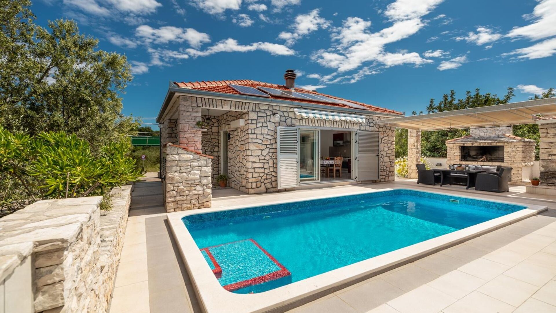 A stone house with a swimming pool, outdoor seating, and a barbecue area.