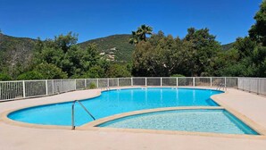 Una piscina de borde curvo, rodeada por una valla blanca, con un fondo de exuberante vegetación y colinas.