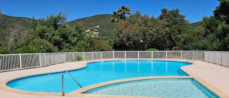 Piscina com borda curva, rodeada por uma cerca branca, com um cenário de vegetação exuberante e colinas.