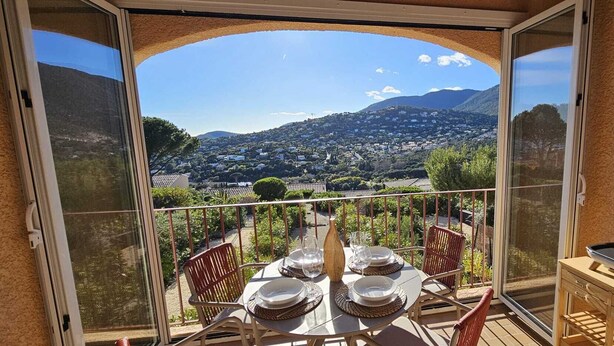 Un balcón con una mesa lista para cuatro personas, con vistas a un paisaje montañoso.