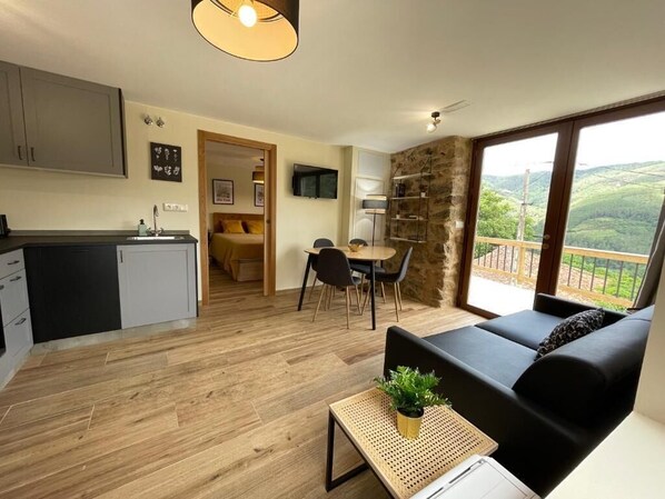 Sala moderna com sofá preto, piso de madeira e varanda com vista.