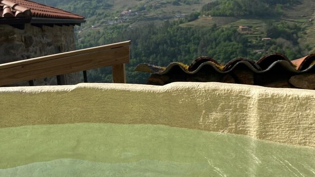 Una piscina cristallina con una panchina di legno e un muro in pietra, con vista su un paesaggio collinare.