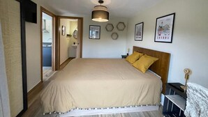 A bedroom with a large bed, a wooden headboard, a bedside table with a lamp, and a wall-mounted light fixture.