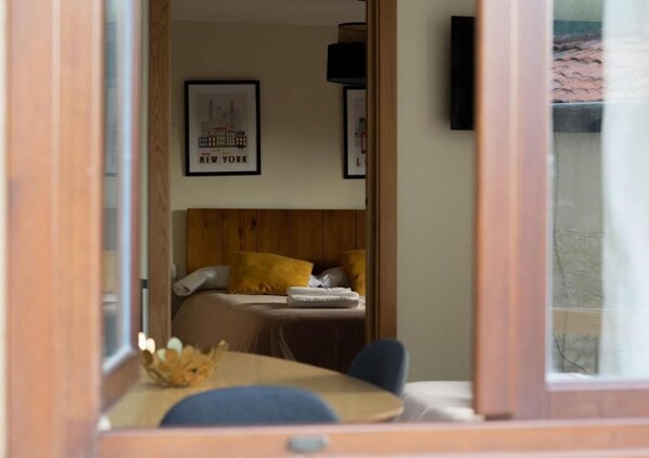 A bedroom with a bed, a wooden headboard, a framed picture of New York, and a window with a view of a building.