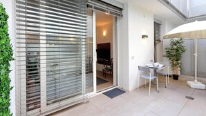 A modern apartment with a sliding glass door leading to a dining area, a small balcony with a table and chairs, and a potted plant. - People's Square Apartment (Roma)