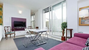 A modern living room with a flat-screen TV, a dining table with chairs, a sofa, and a large window with blinds. - People's Square Apartment (Roma)
