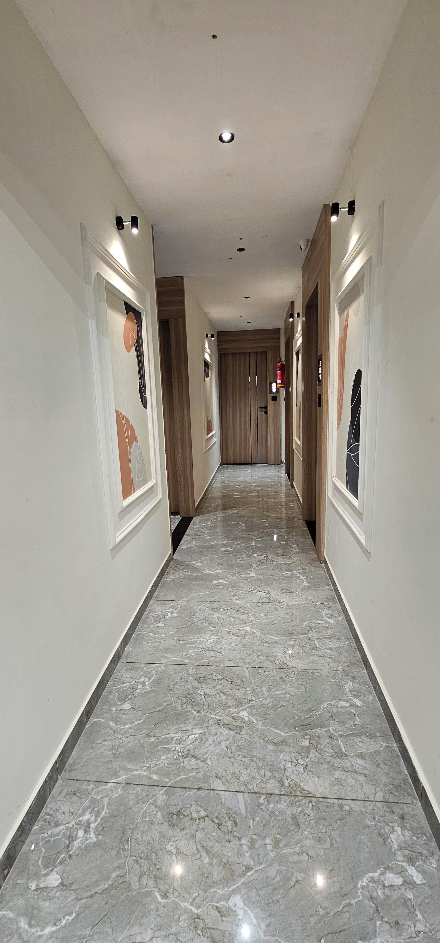A hallway with marble flooring, wooden doors, and wall-mounted light fixtures.