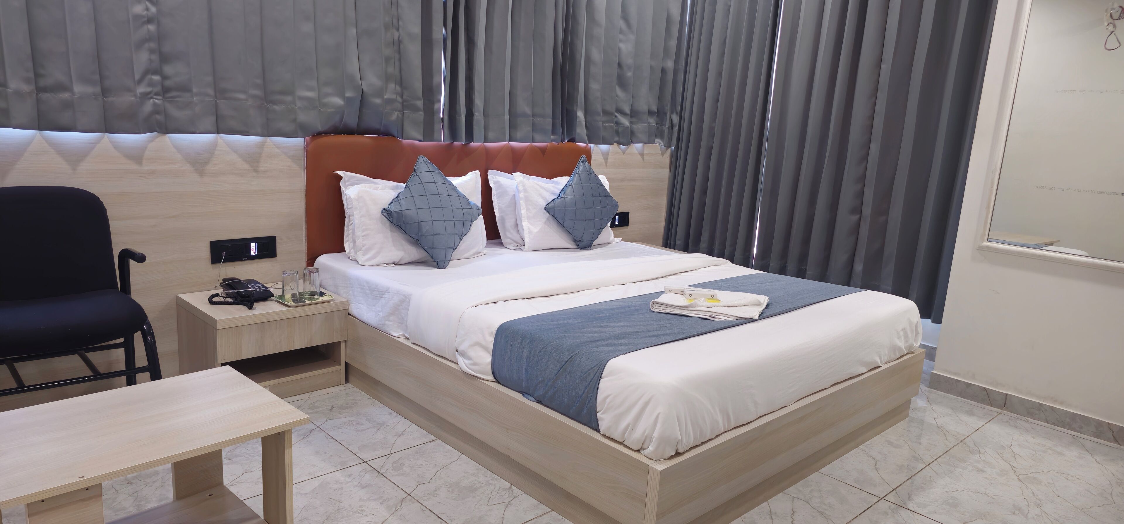 A neatly arranged hotel room with a bed, bedside table, chair, and a small table.