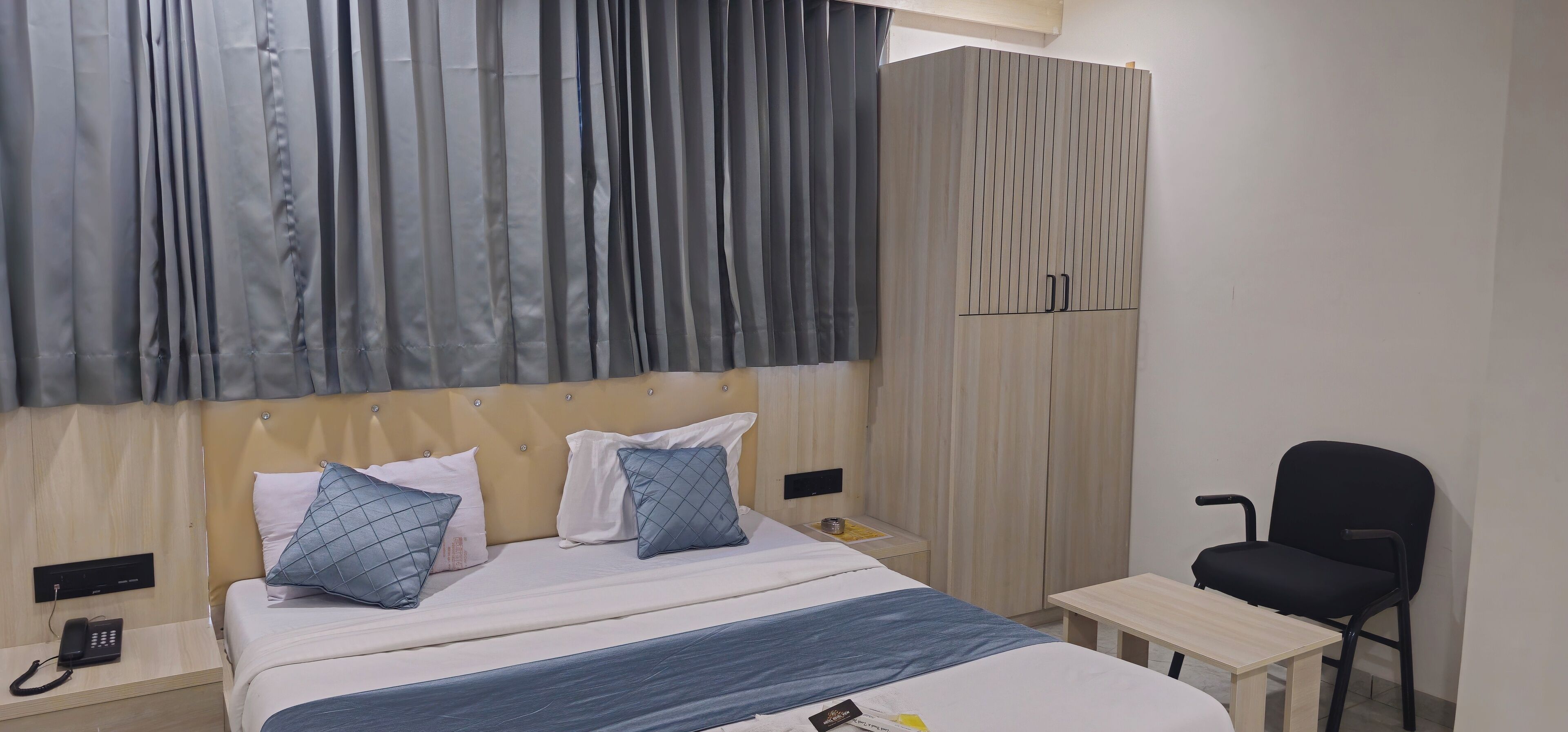 Une chambre d’hôtel comprenant un lit, une table de chevet avec un téléphone, une chaise et une armoire.