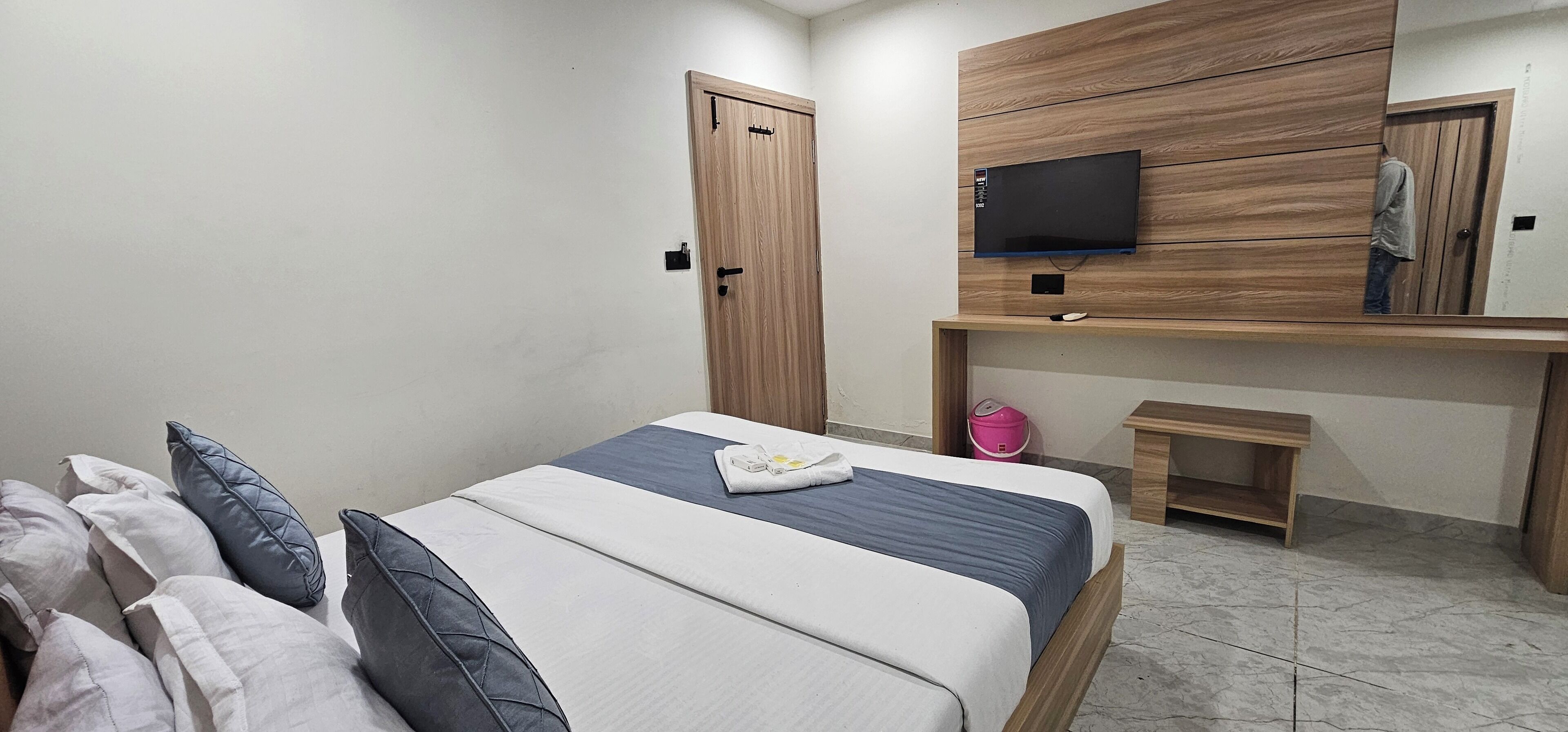 Una camera da letto con un letto, una TV montata su una parete in legno, una scrivania in legno e uno sgabello.
