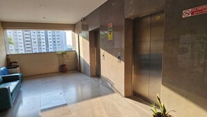 A modern lobby with a sofa, a potted plant, and an elevator. - HOTEL ROYAL VIEW (Ahmedabad)