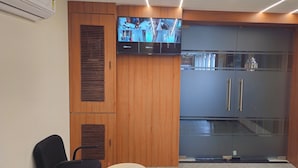 A modern hotel room with a large flat-screen TV mounted on the wall, a wooden wardrobe, and a sliding glass door. - HOTEL ROYAL VIEW (Ahmedabad)