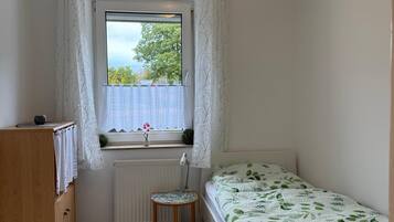Ein kleines, ordentliches Schlafzimmer mit einem Einzelbett, einem Holzschrank, einem Heizkörper und einem Fenster mit Vorhängen.
