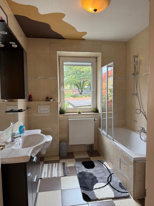 A bathroom with a window, a bathtub, a shower, and a sink.