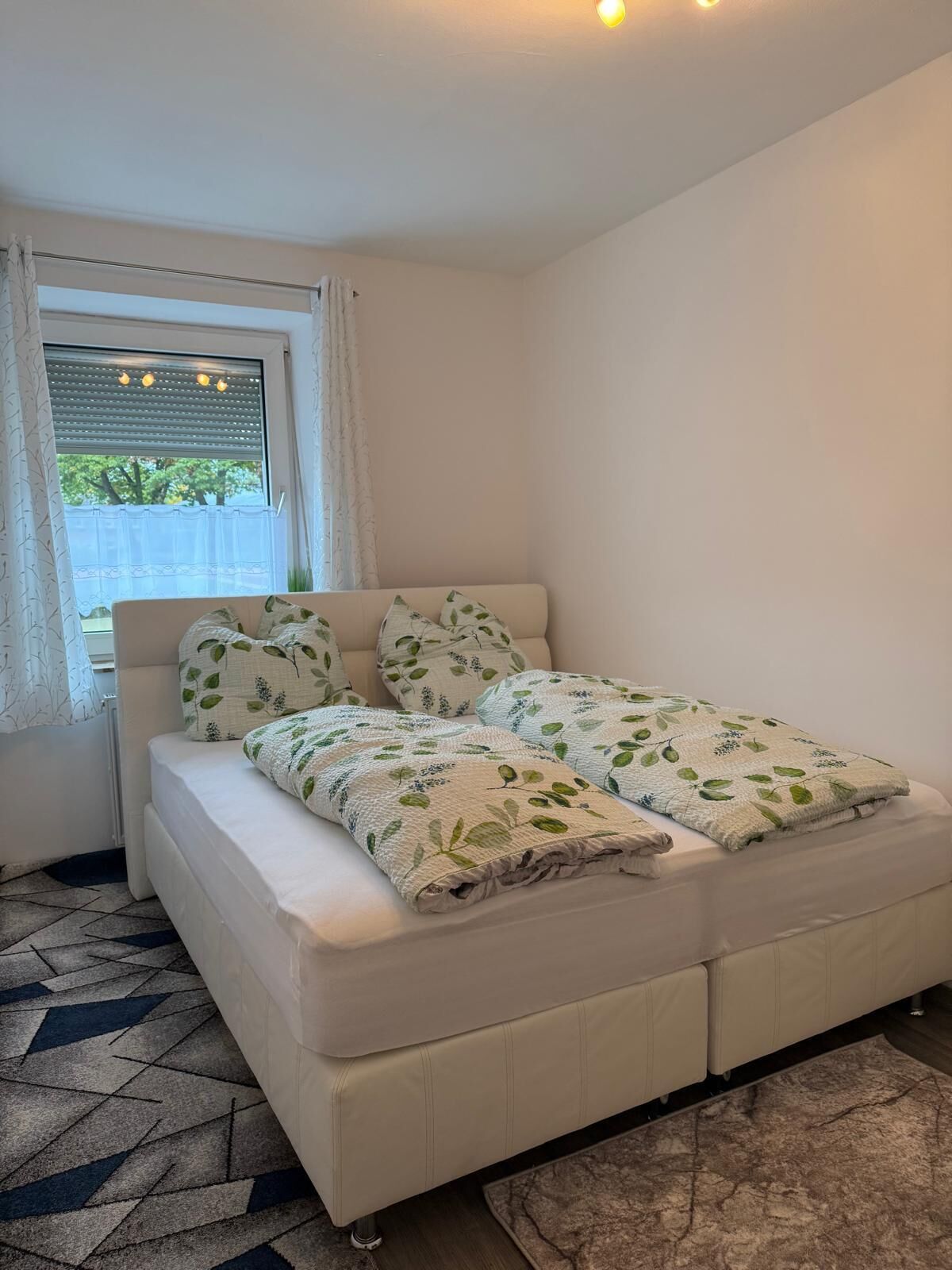 A bedroom with a bed, a window with blinds, and a patterned rug.