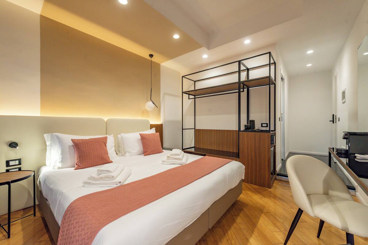A modern hotel room with a large bed, a wooden desk, and a chair.
