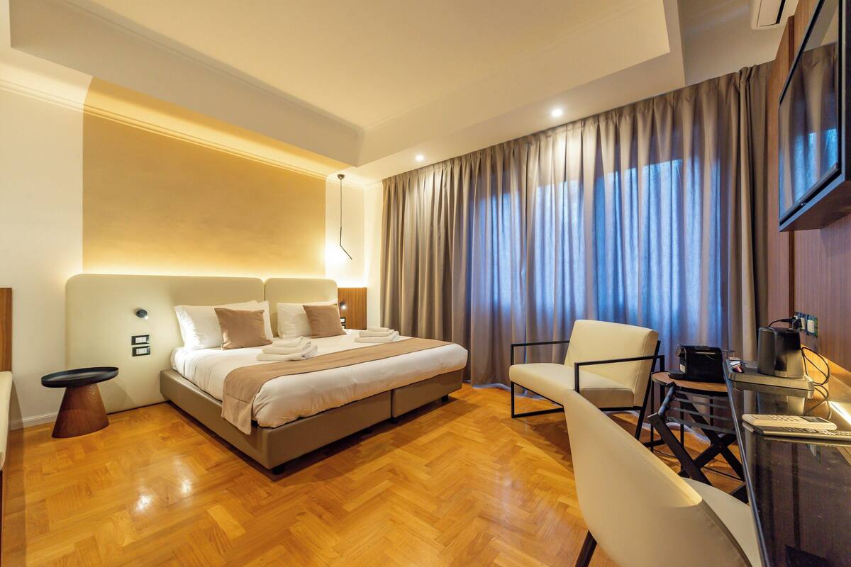 A hotel room with a large bed, a desk with a computer, a chair, and a TV.