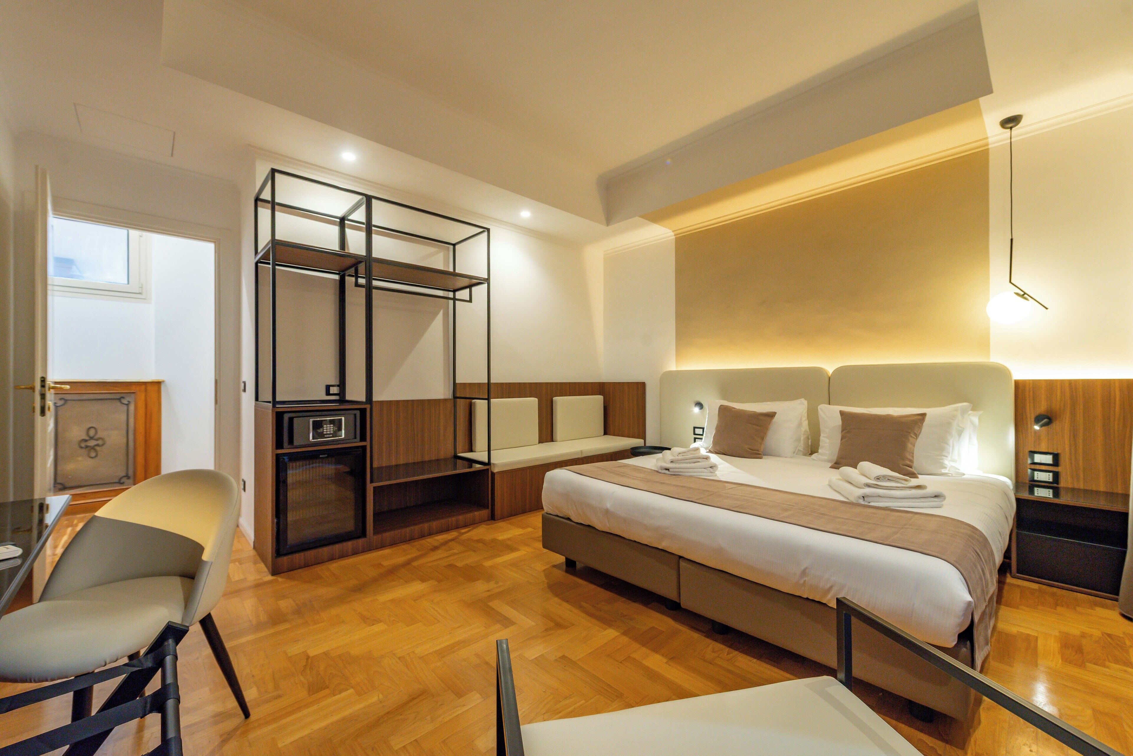 A modern hotel room with a large bed, a seating area, and a built-in wardrobe.