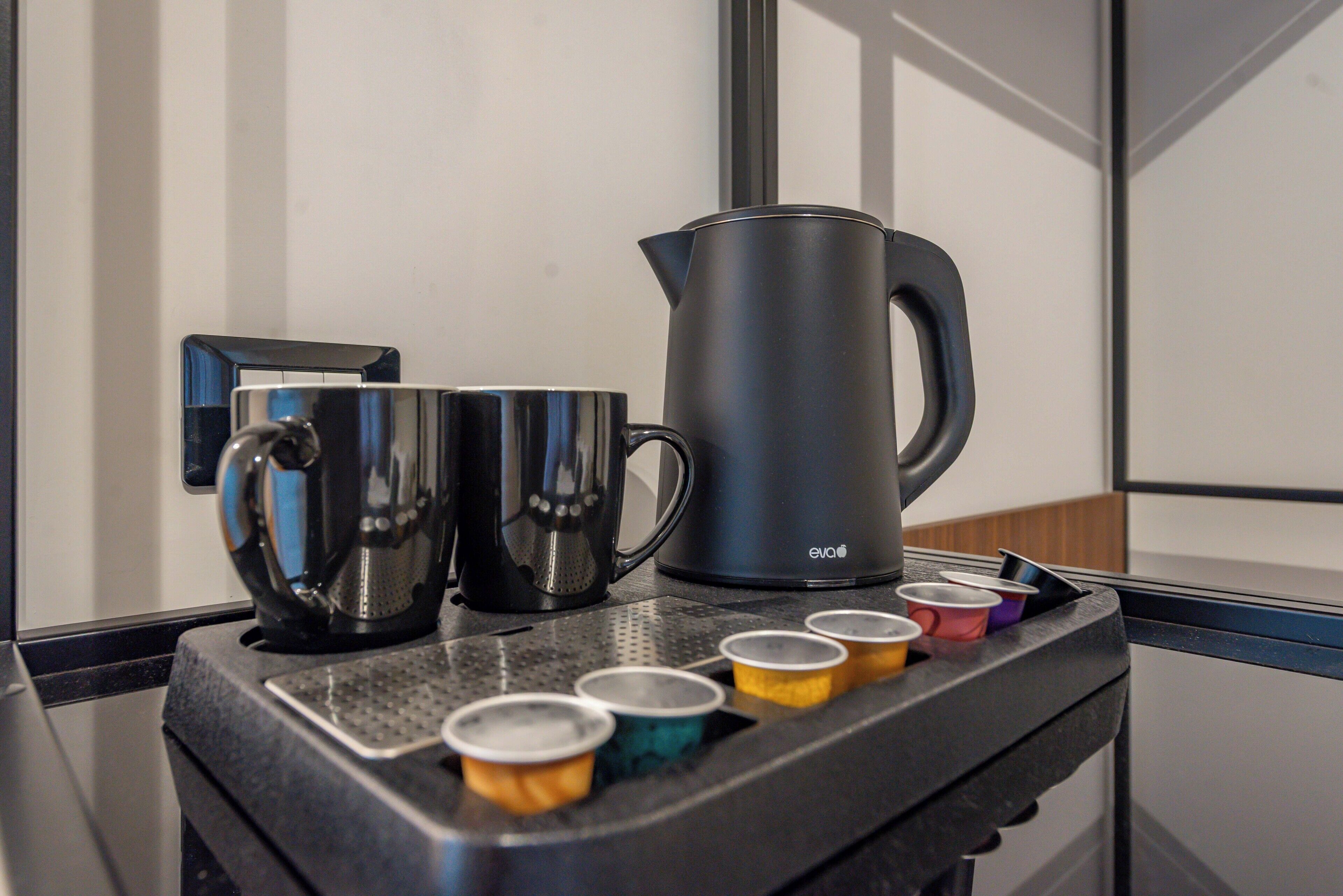 A coffee station with a black coffee maker, two stainless steel cups, and several colorful disposable cups.