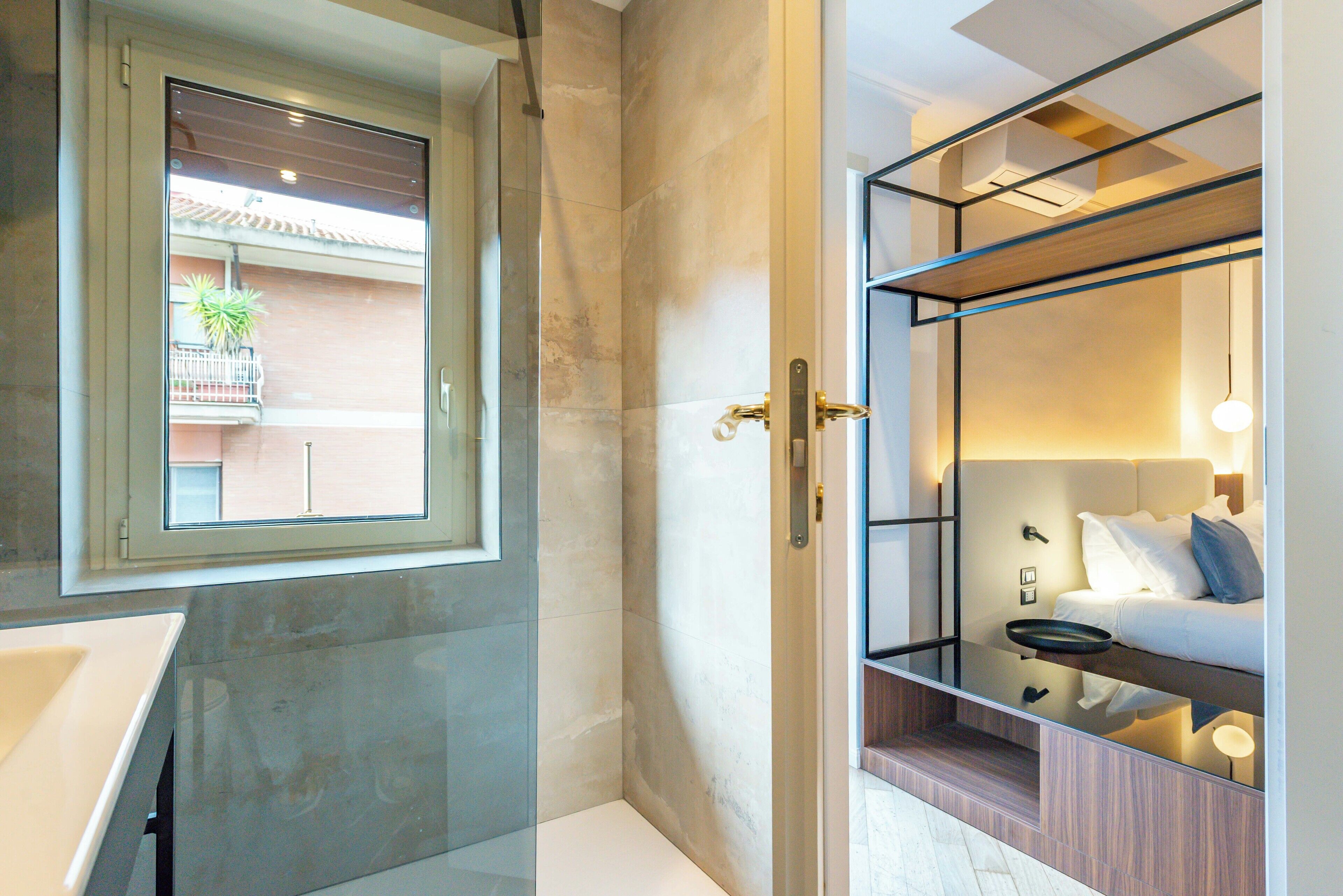 Un bagno moderno con cabina doccia in vetro, un lavandino e una finestra con vista su un balcone fiorito.