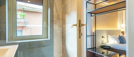 Un bagno moderno con cabina doccia in vetro, un lavandino e una finestra con vista su un balcone fiorito.