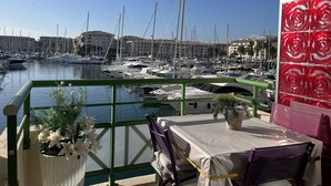 Ein Balkon mit Tisch und Stühlen mit Blick auf eine Marina, im Hintergrund Schiffe und Gebäude.