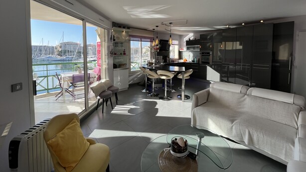 Ein modernes Wohnzimmer mit einer Couch, einem Glastisch und Blick auf den Hafen durch große Fenster.