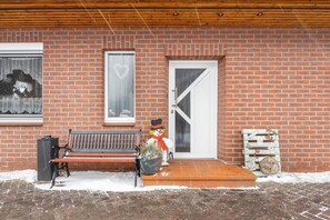 A brick building with a wooden bench, a door, and a snowman decoration. - Apartment 'Kehdingen' with Private Terrace and Wi-Fi (Drochtersen)