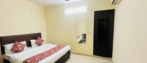 A hotel room with a bed, a ceiling fan, an air conditioning unit, and a door.