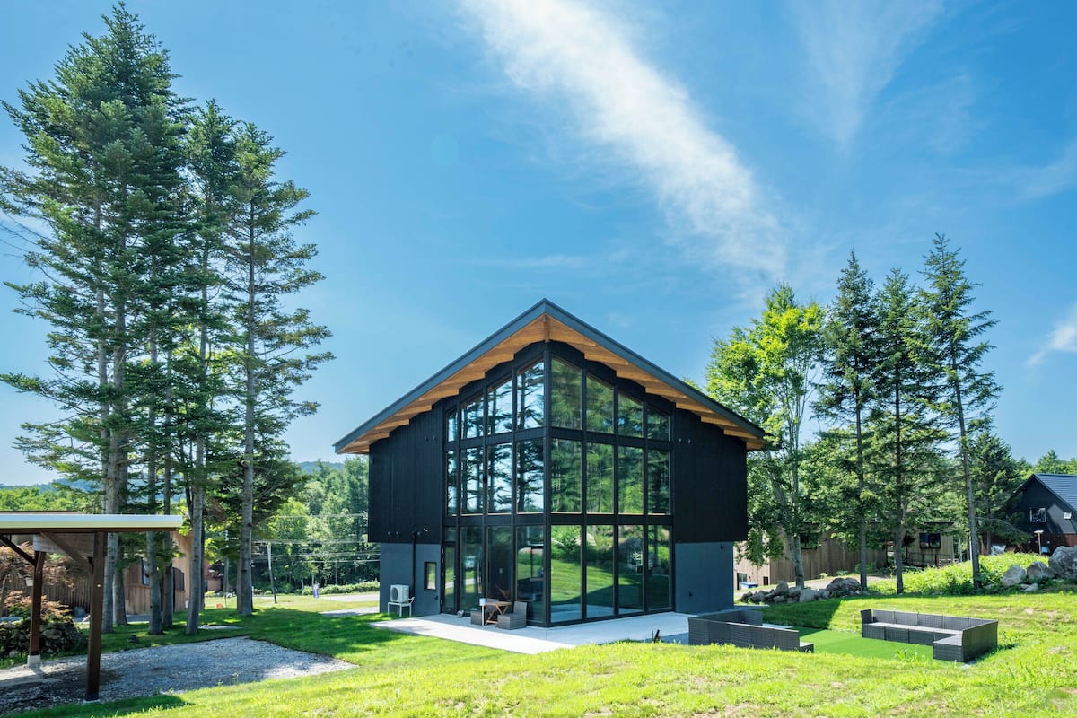 A modern house with large glass windows, a wooden roof, and a well-maintained lawn.