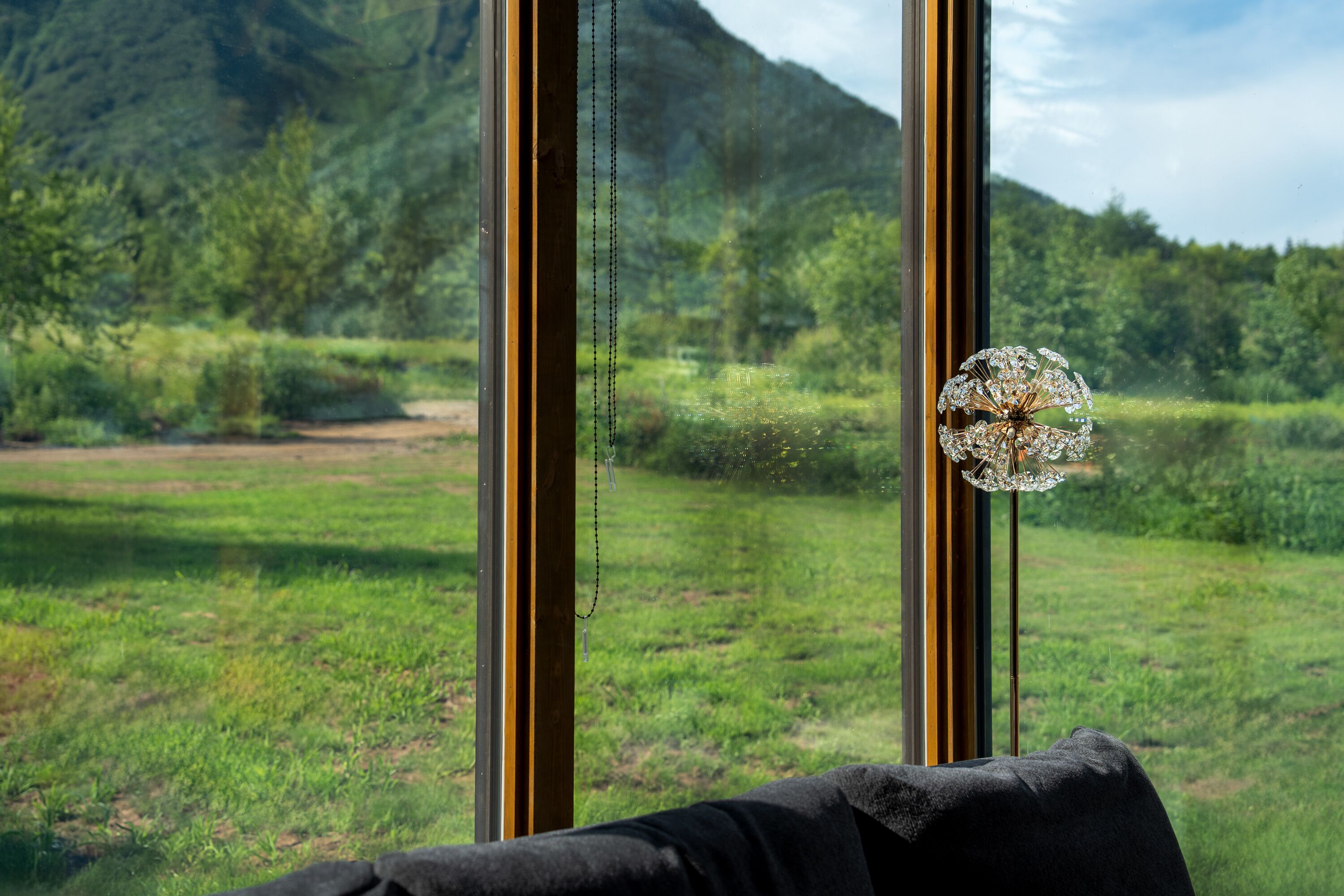 A room with a large window overlooking a grassy field and a mountain.