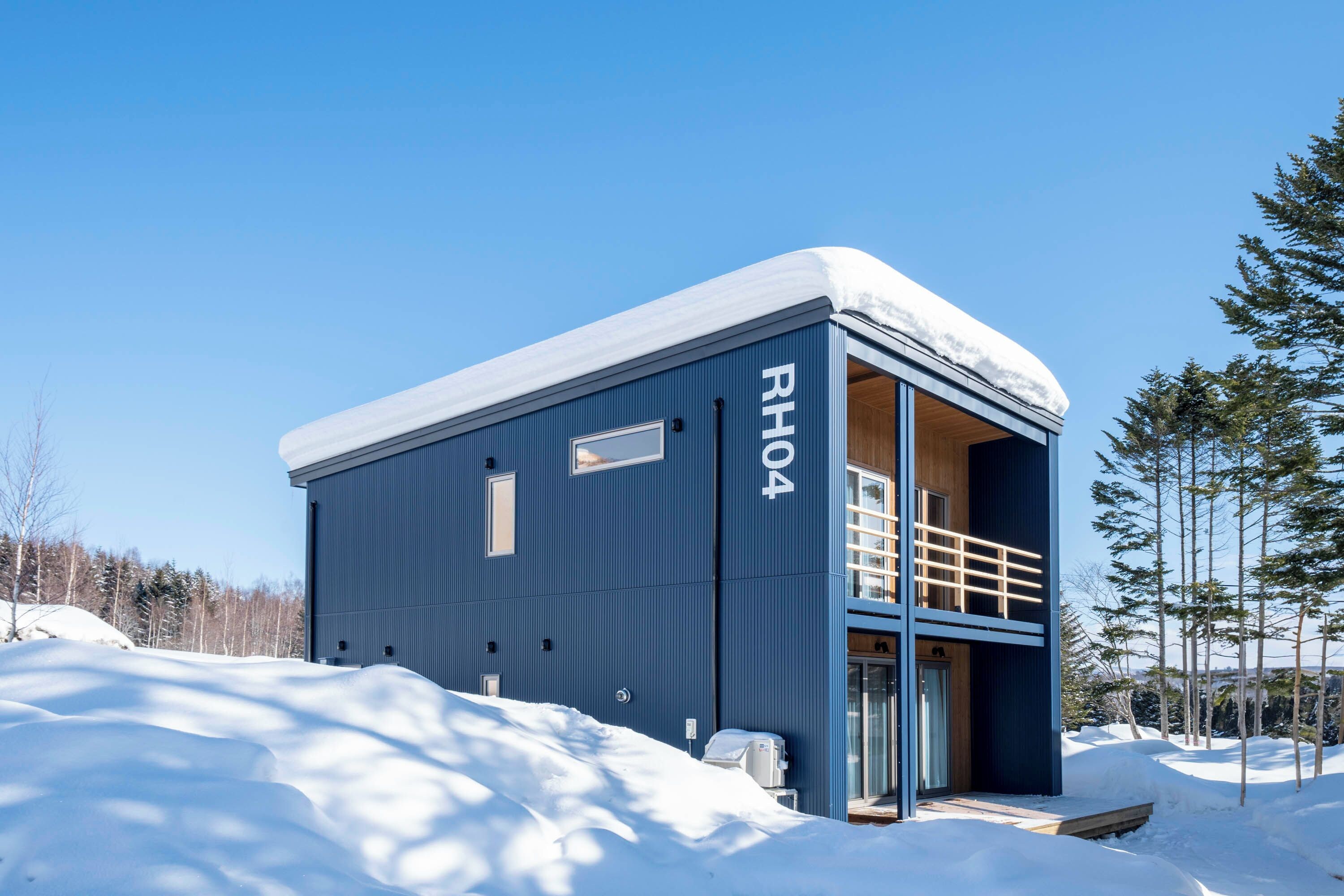 A modern, blue building with the number RH04 on its side, featuring a balcony and a wooden door.