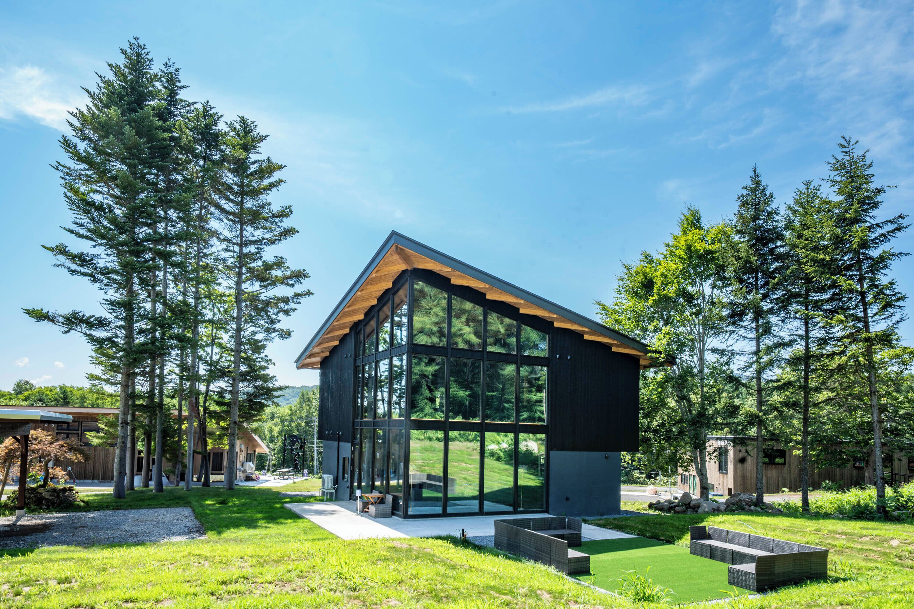 A modern house with large glass windows, surrounded by a well-maintained lawn and tall trees.