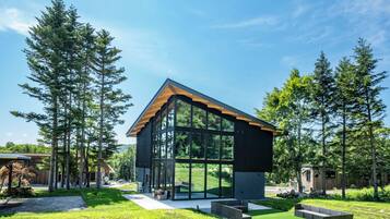 A modern house with large glass windows, surrounded by a well-maintained lawn and tall trees.