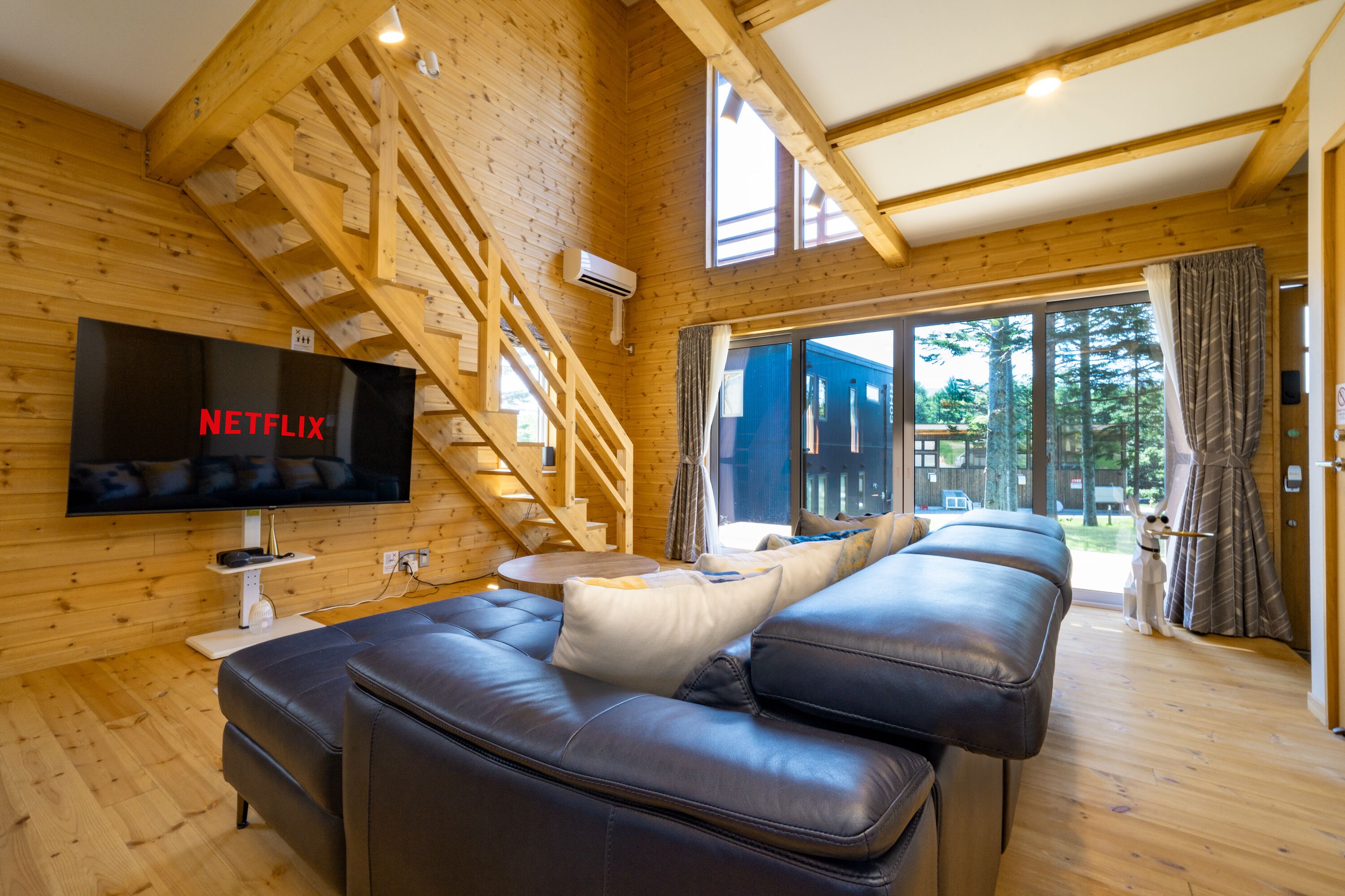 Ein gemütliches Holzhaus-Interieur mit großem Fernseher, einer Treppe und einer Couch.