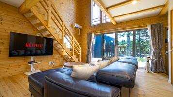 Ein gemütliches Holzhaus-Interieur mit großem Fernseher, einer Treppe und einer Couch.