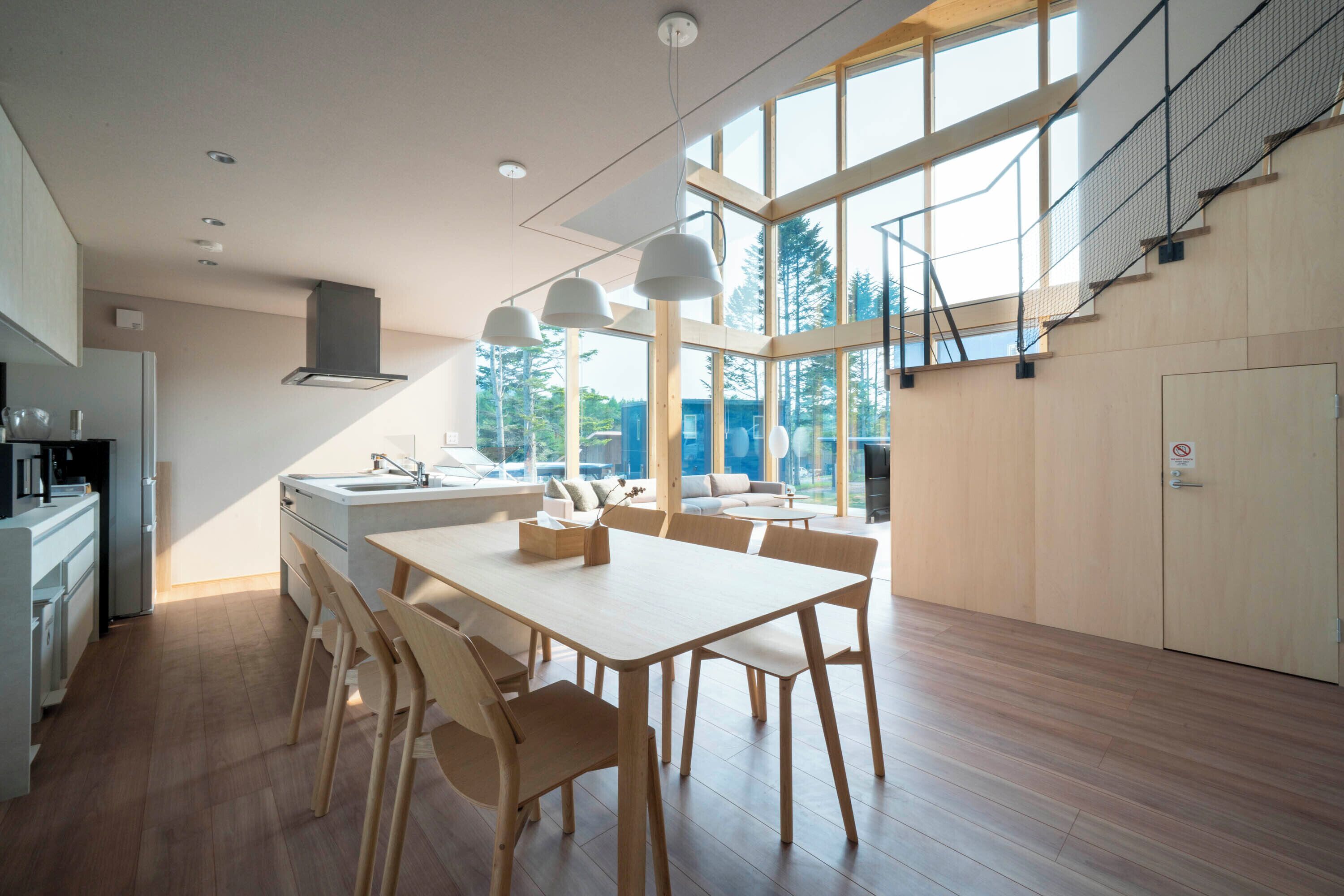 A modern kitchen with a large island, wooden chairs, and pendant lighting.