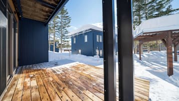 A wooden deck with snow on the ground, a blue building, and a covered area with snow.