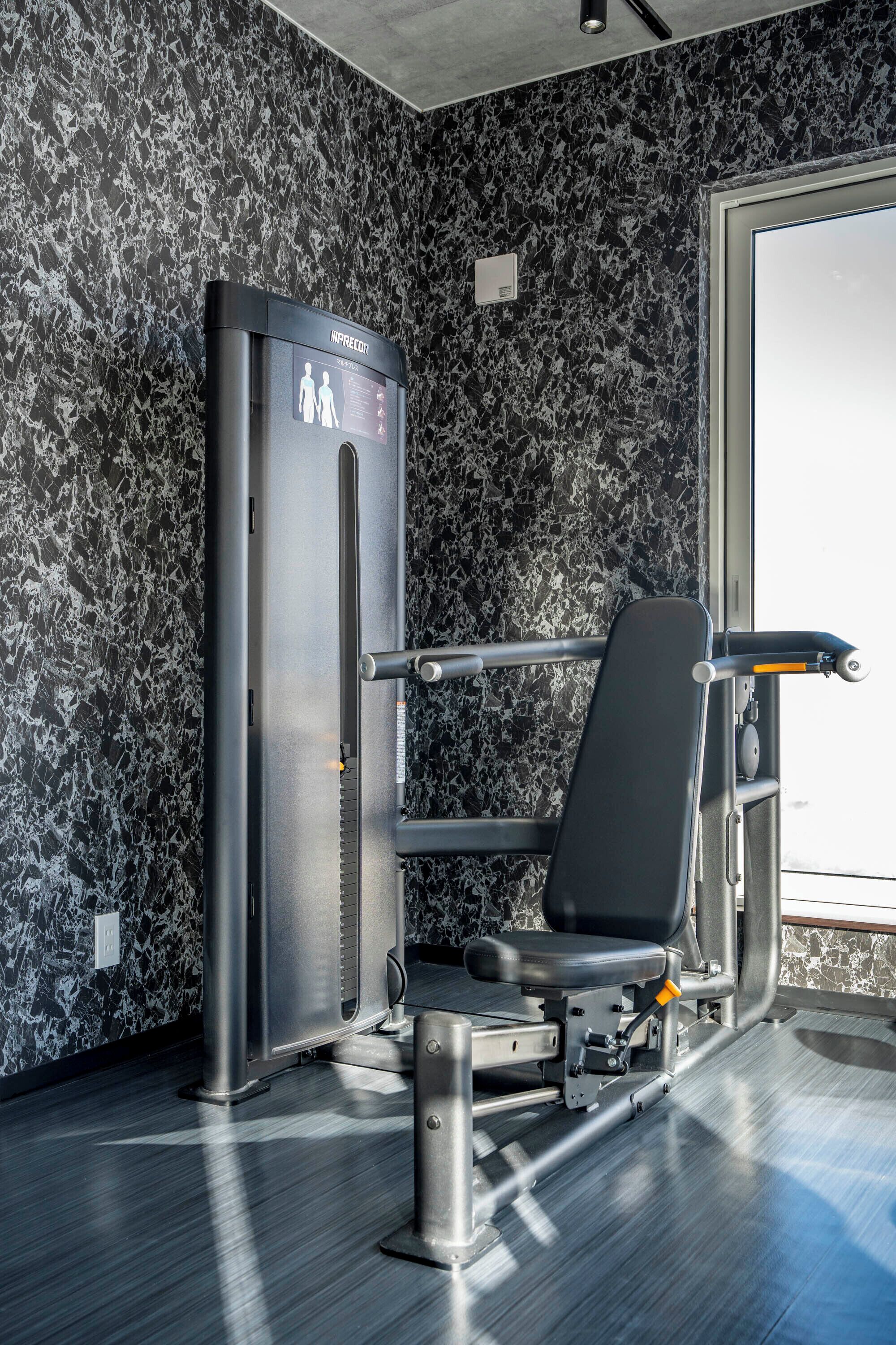 Ein Fitnessraum mit einem an der Wand befestigten Trainingsgerät, einer Bank und einer Tür.