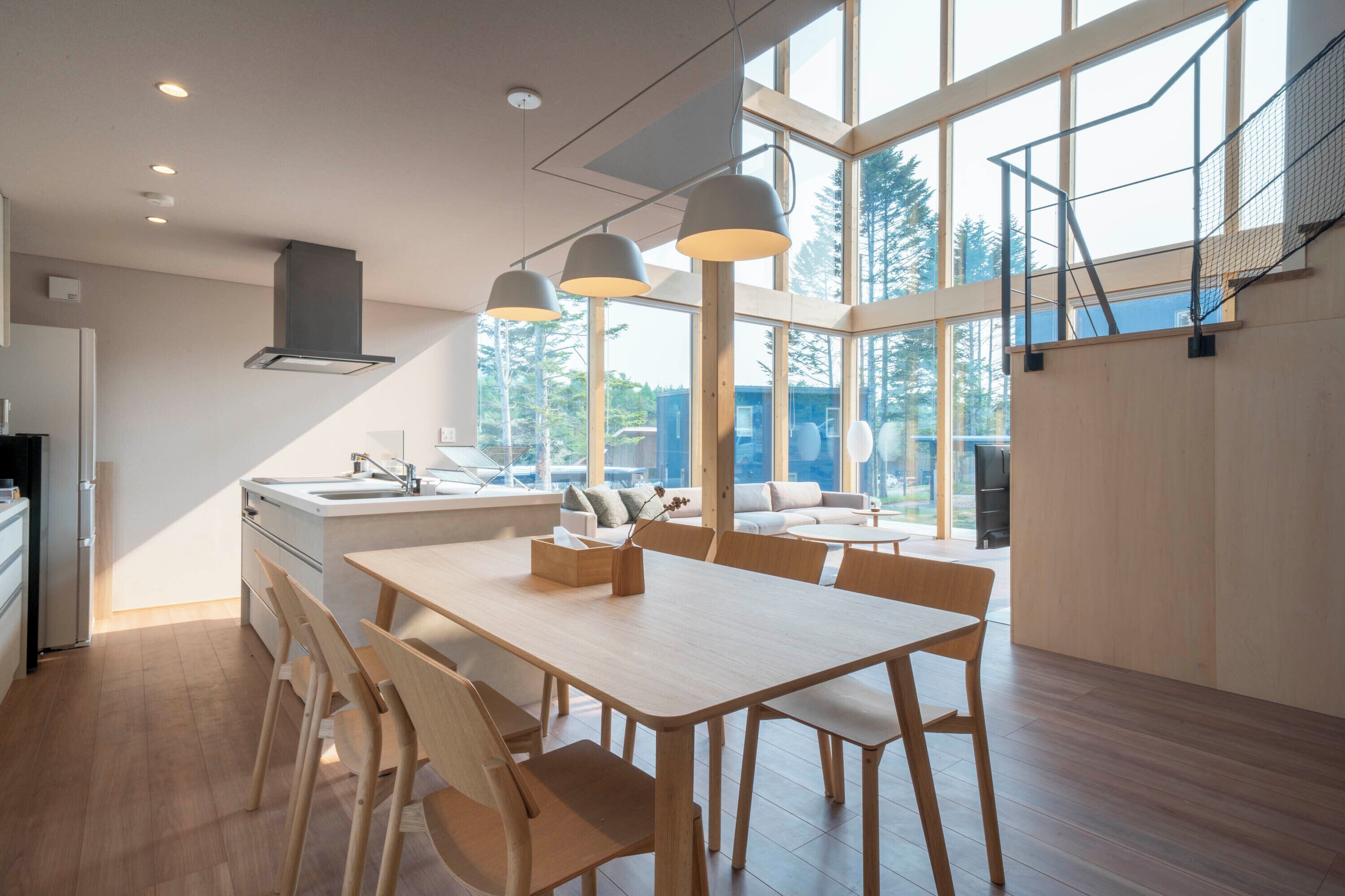 A modern kitchen with a dining area, large windows, and a staircase.