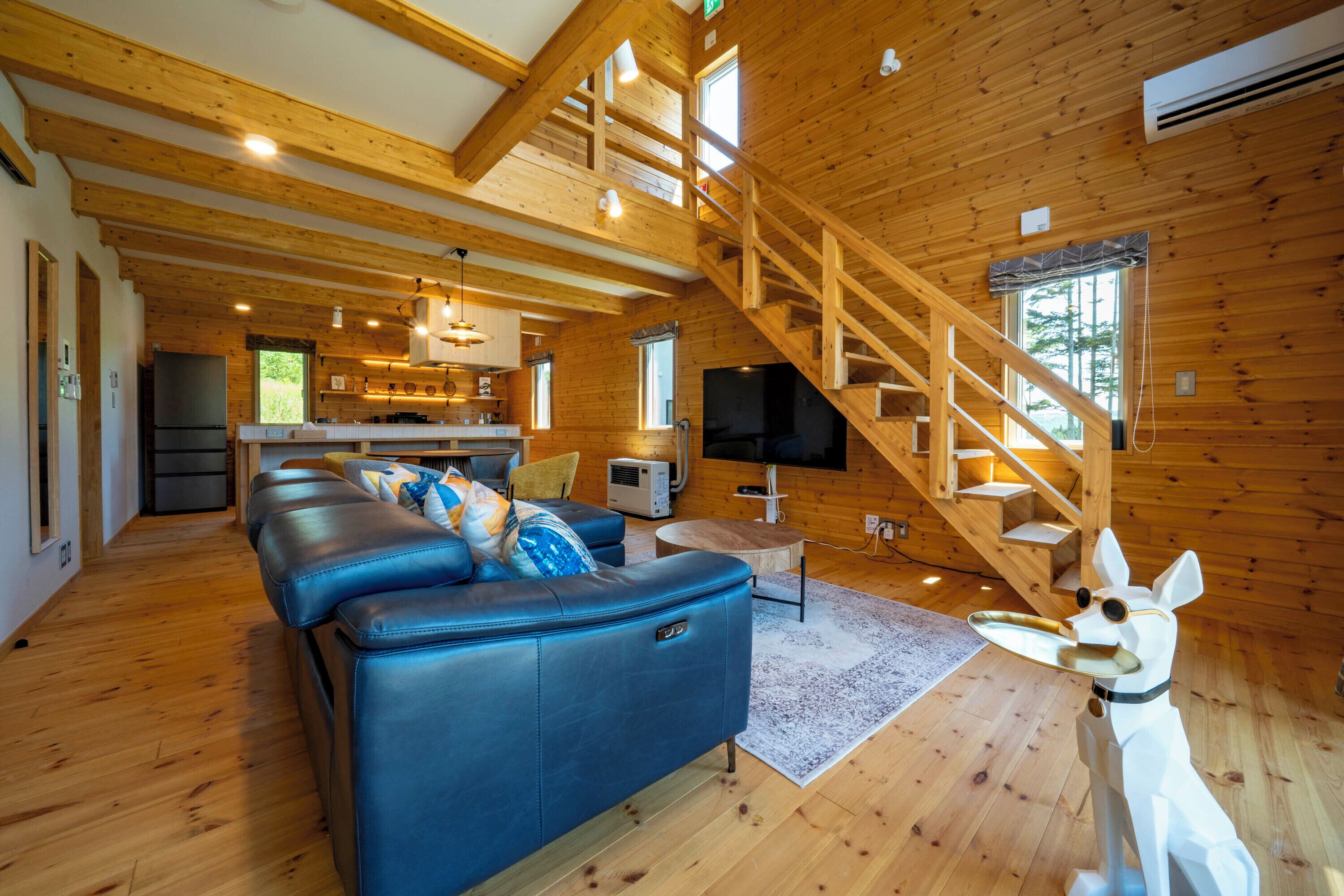 A wooden cabin interior with a living room, kitchen, and staircase.
