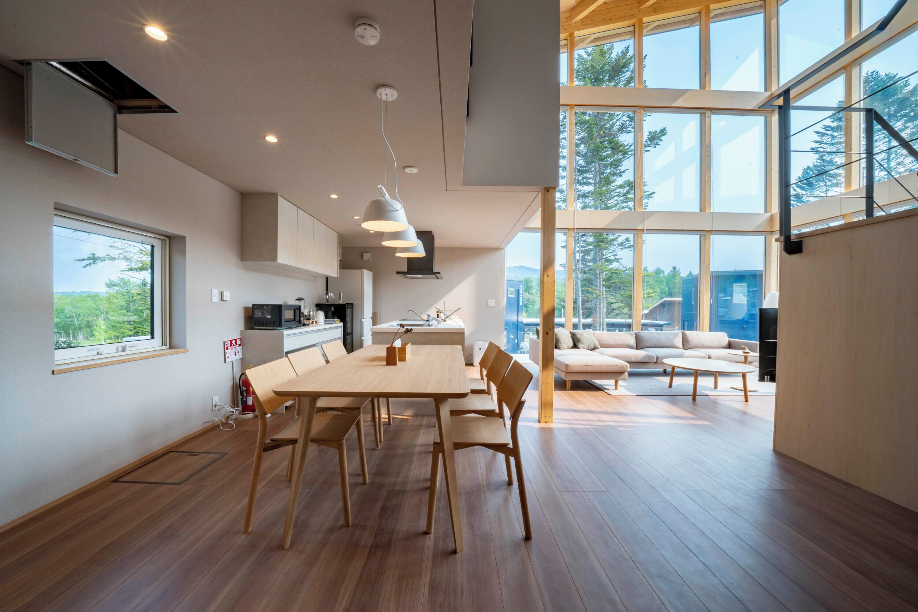 A modern kitchen with a dining area, large windows, and a view of the outdoors.