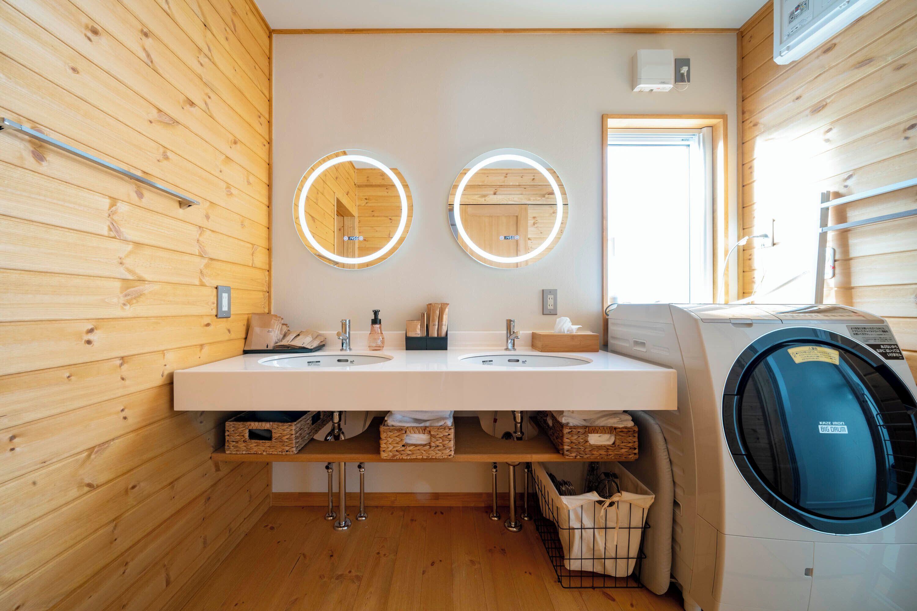 Een moderne badkamer met houten lambrisering, twee wastafels met manden eronder, een wasmachine en een spiegel met verlichting.