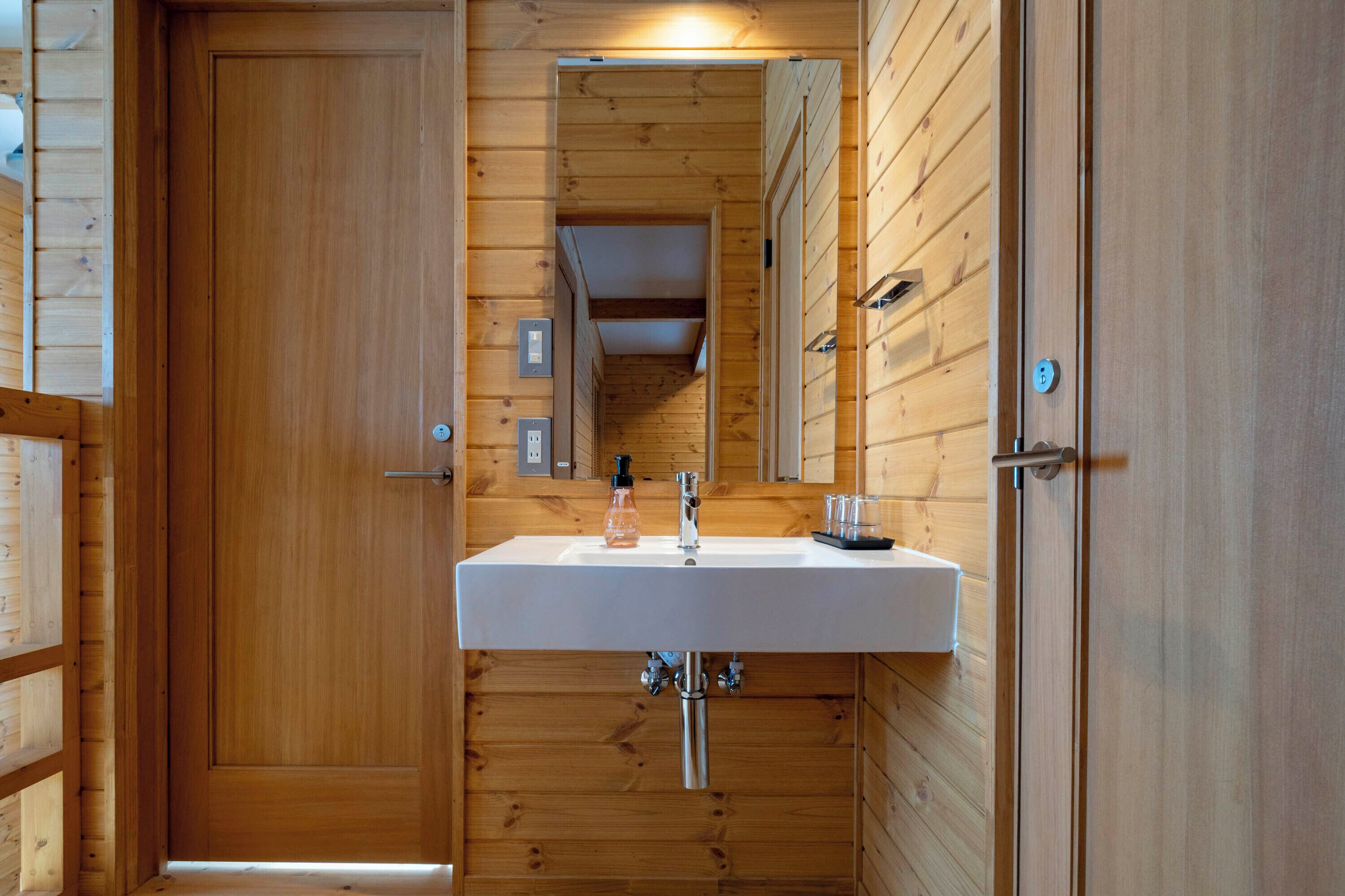 A wooden-paneled bathroom with a white sink, a mirror, and a door.