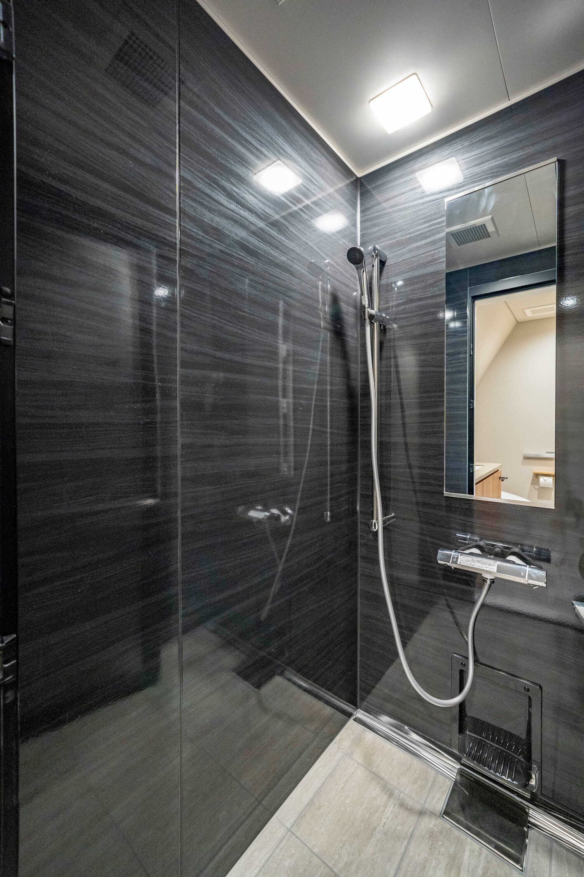 A modern bathroom with a glass shower enclosure, a built-in mirror, and a sleek, dark-tiled wall.