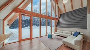 Un interior moderno con un ventanal grande, pisos de madera, un sofá blanco y una mesita.