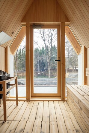 Una cabaña de madera con una puerta grande abierta que da a una vista de árboles y un cuerpo de agua.