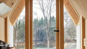 Una cabaña de madera con una puerta grande abierta que da a una vista de árboles y un cuerpo de agua.